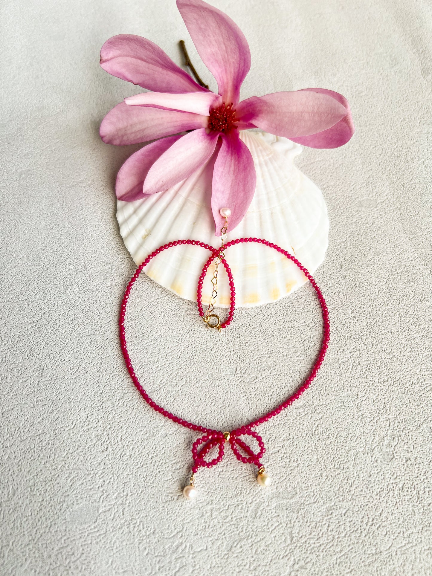 Pink gemstones choker necklace with a knot on a big shell next to a pink flower