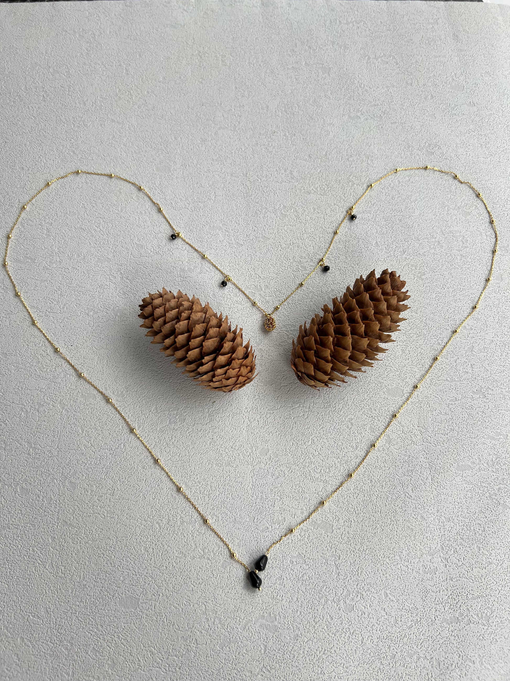 Pinecone layered necklace laid out a heart shape with 2 pinecones in the middle