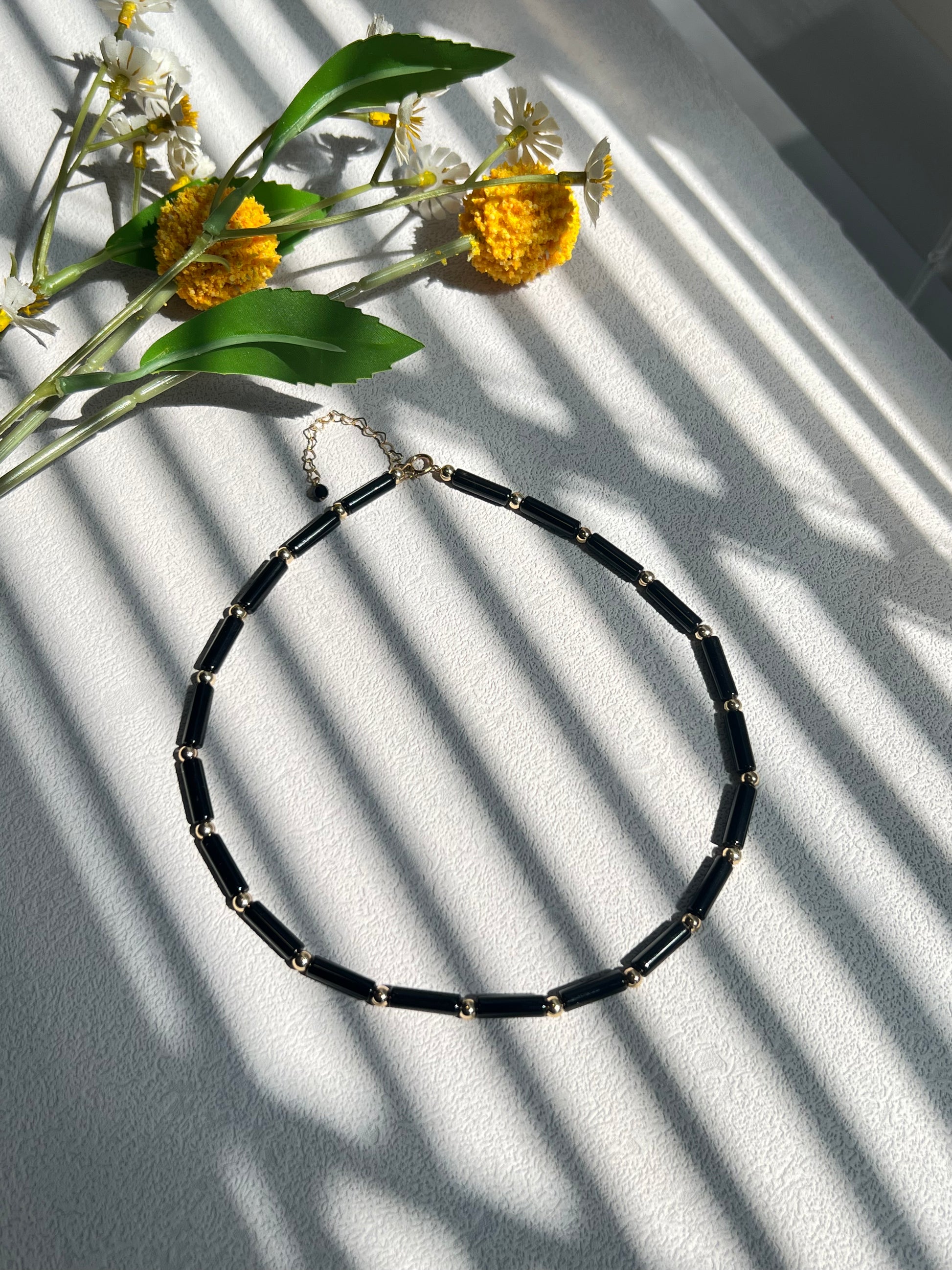 Black agate choker necklace next to yellow flowers