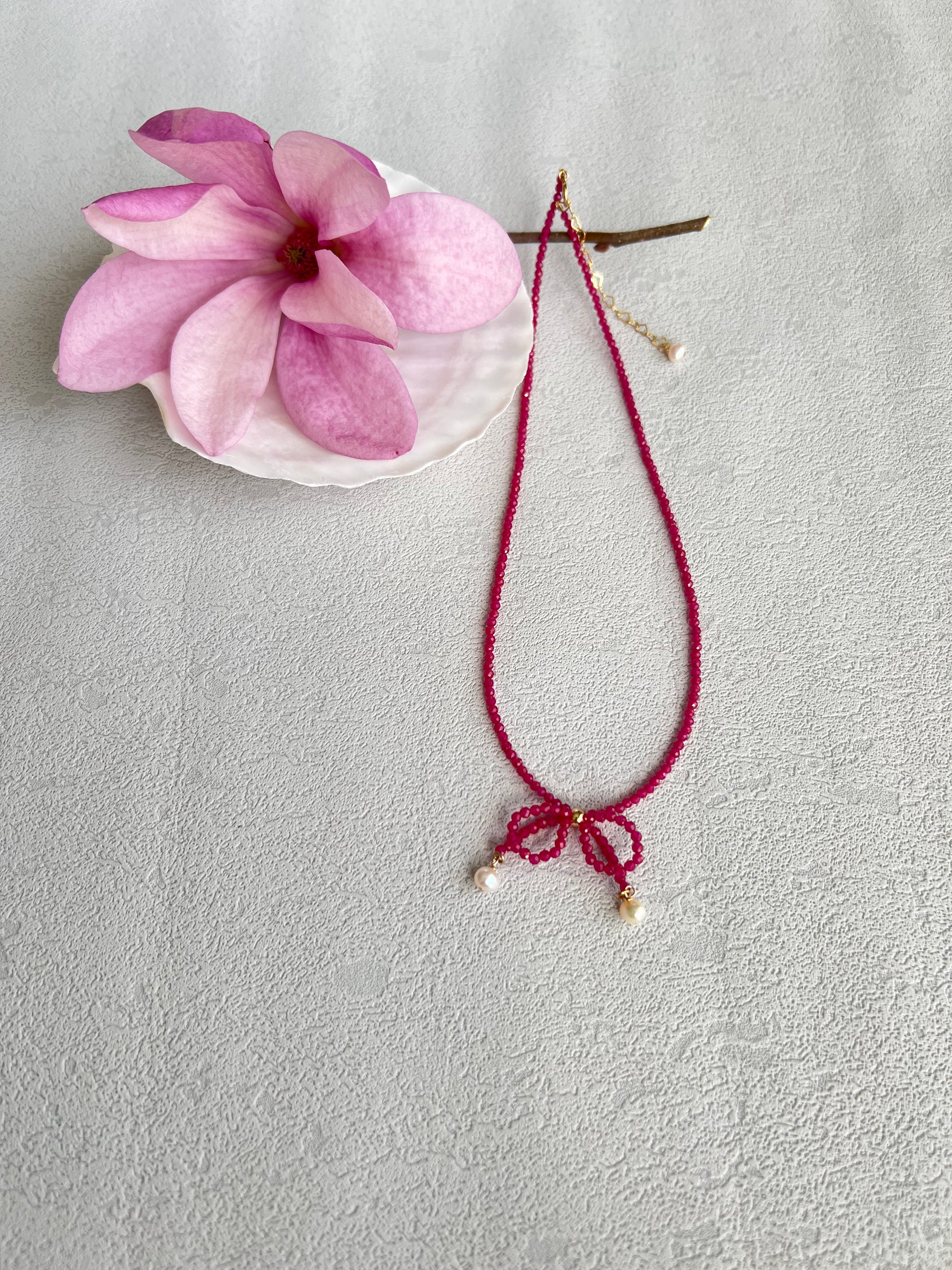 Pink gemstones choker necklace with a knot next to a pink flower