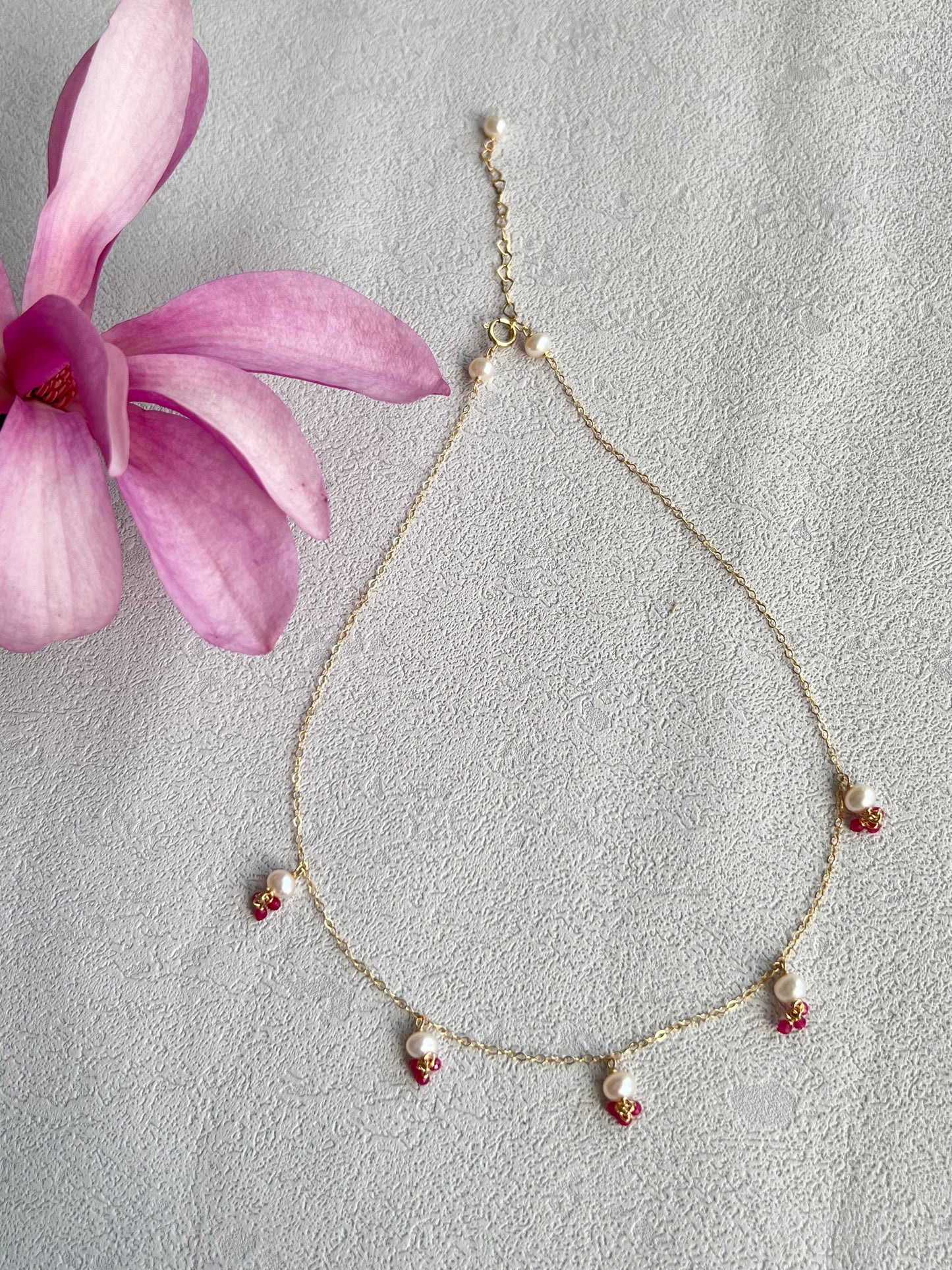 Pink gemstones & pearls necklace next to a pink flower