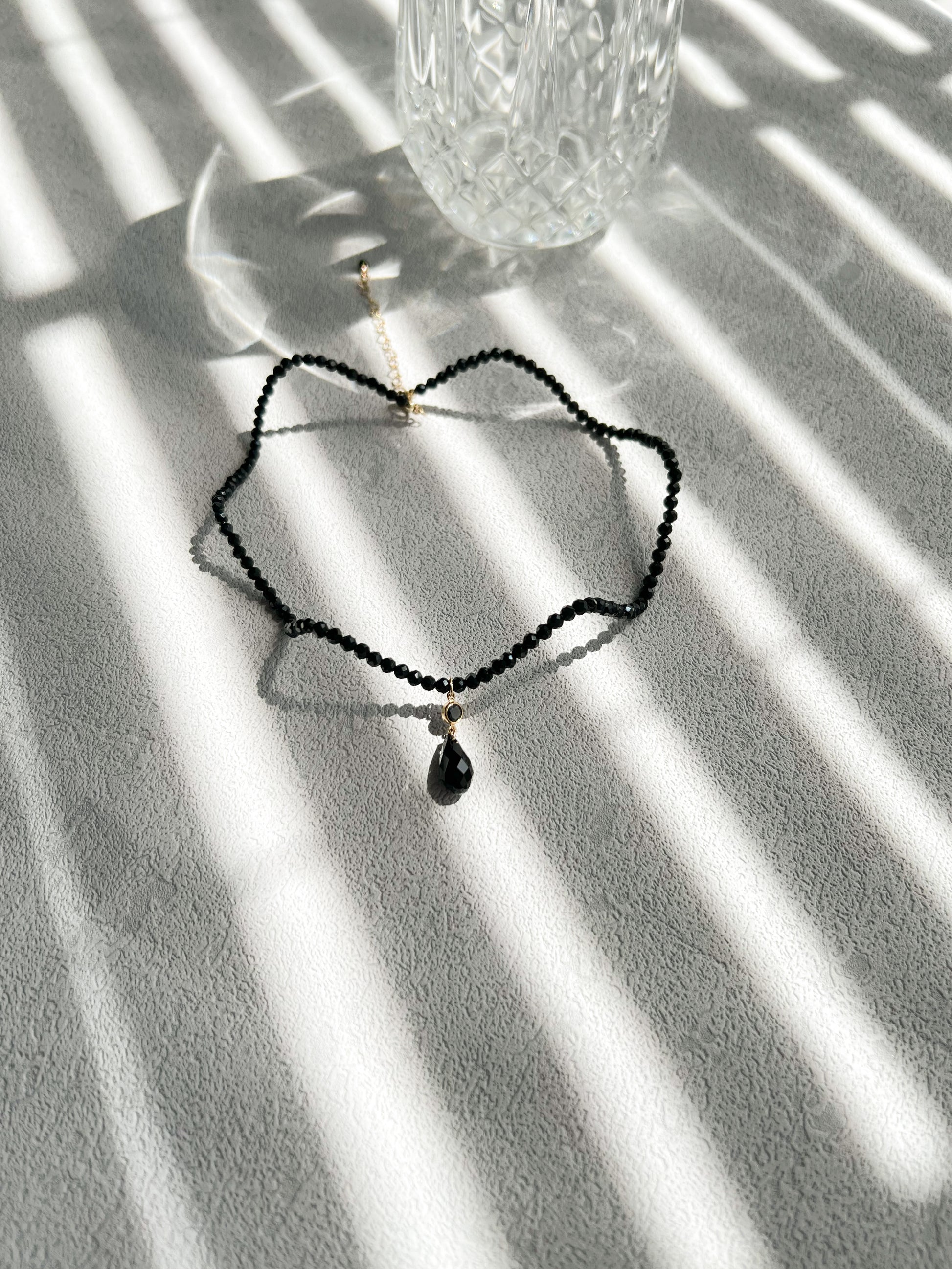 Black wave curve crystal choker necklace next to a glass