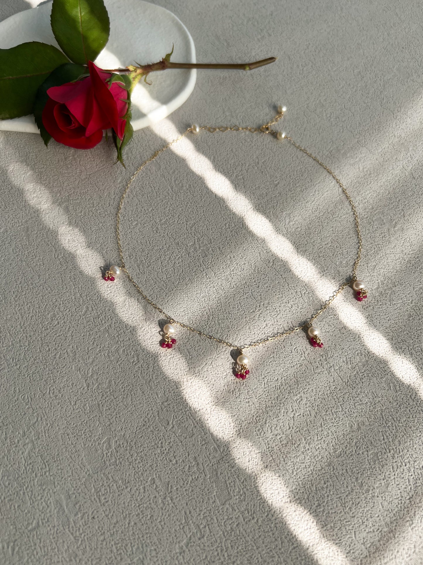 Pink gemstones & pearls necklace next to a rose