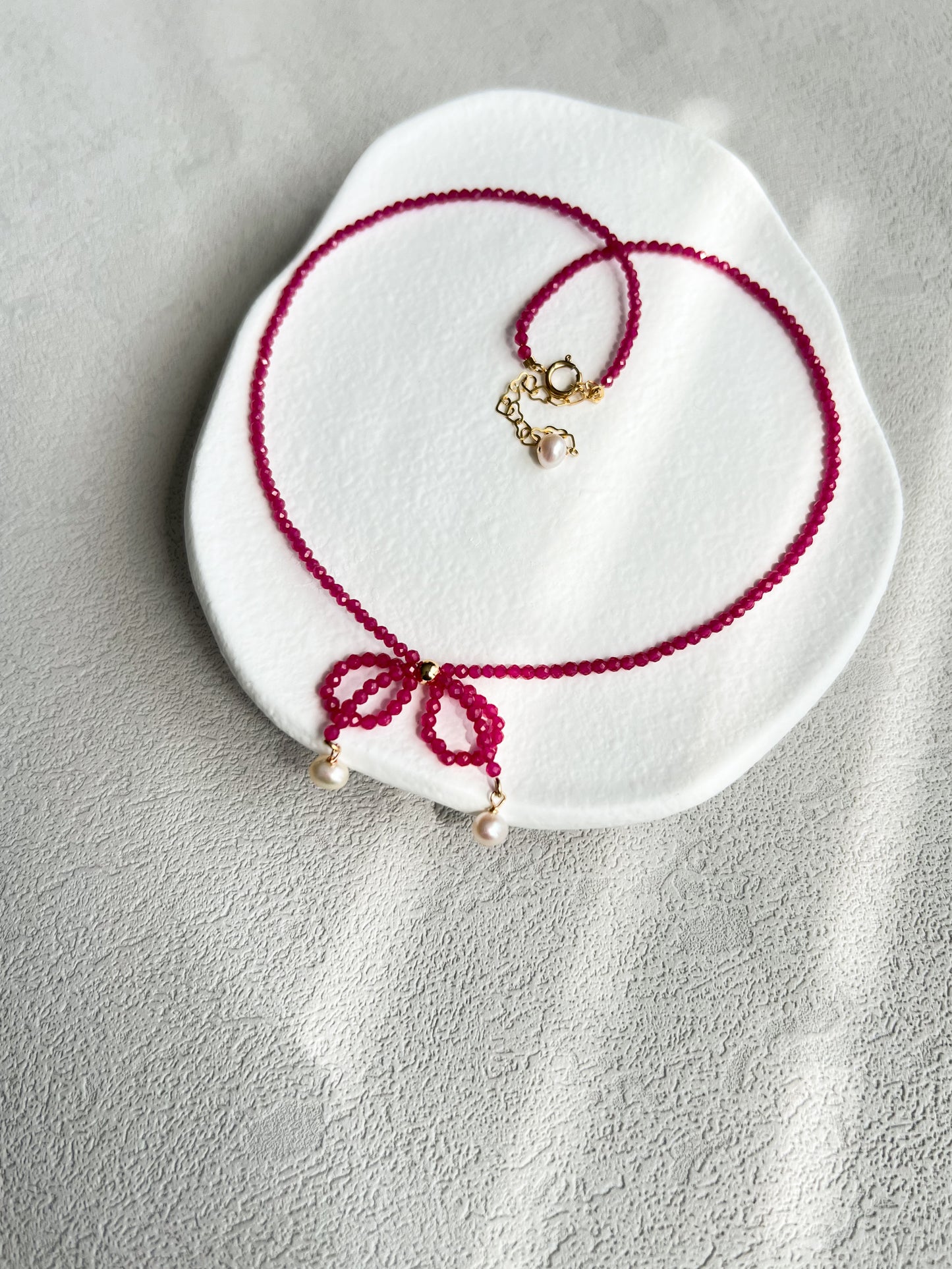 Pink gemstones choker necklace with a knot on a white plate