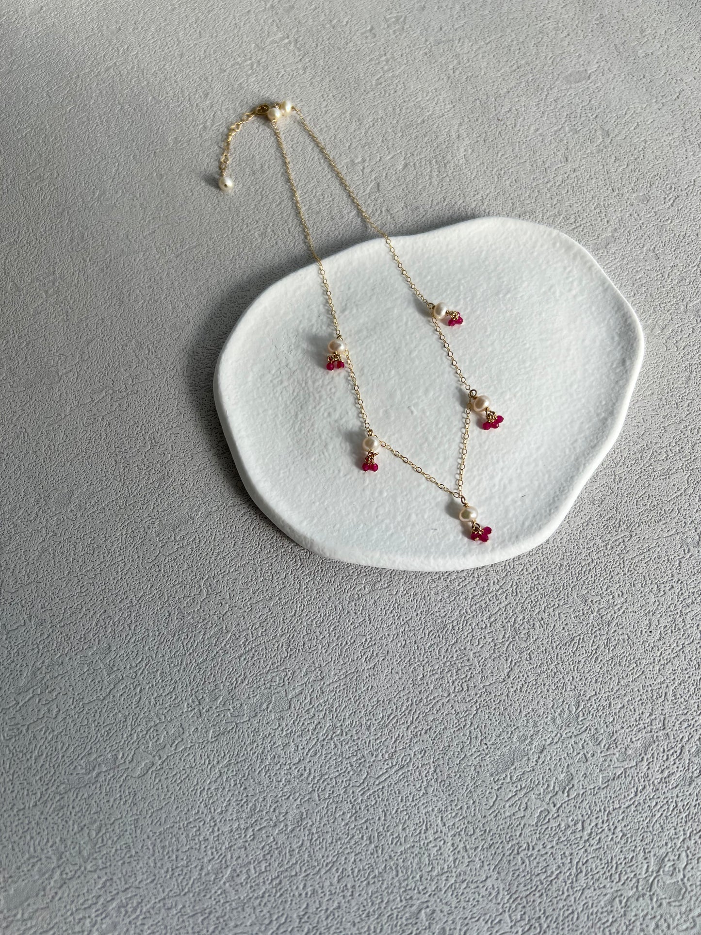 Pink gemstones & pearls necklace on a white plate