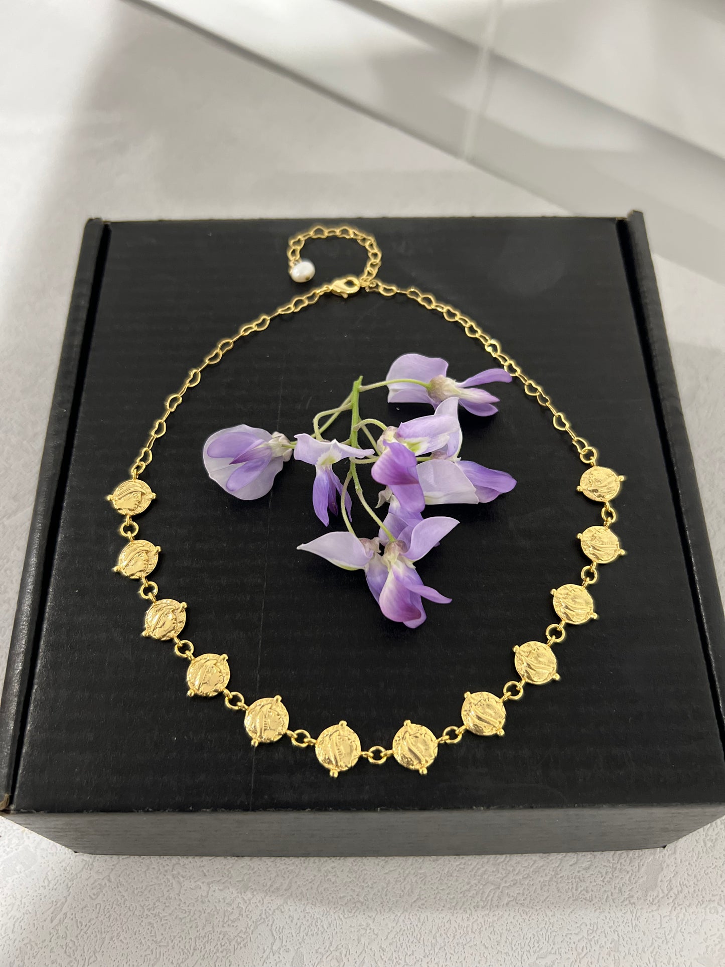 24k gold plated cascading coin choker necklace on a black box with purple flowers in the middle