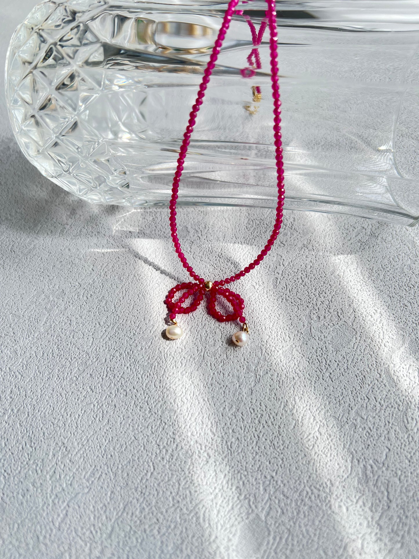 Pink gemstones choker necklace with a knot over a crystal clear glass