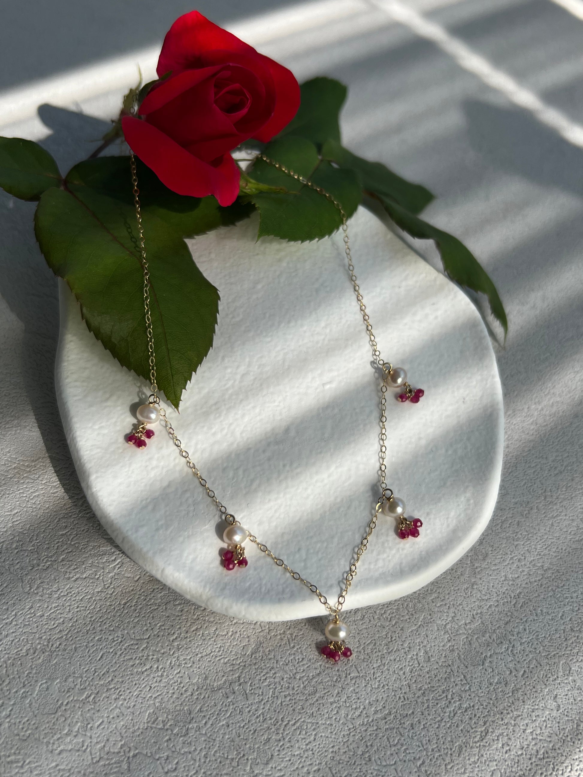 pink gemstones & pearls necklace next to a rose