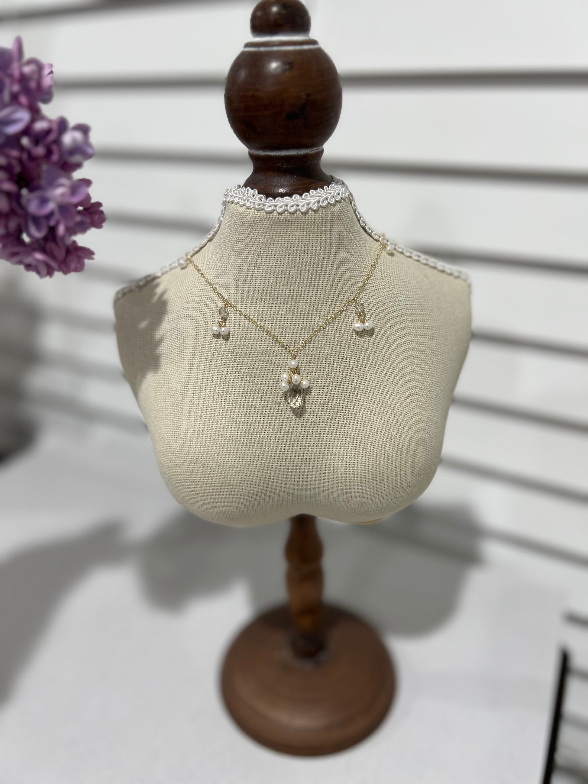 Swarovski crystal & pearls necklace on a small mannequin next to purple flowers